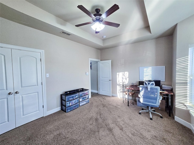 carpeted office space with a tray ceiling and ceiling fan