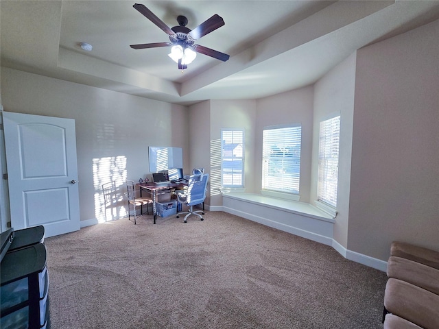 carpeted office featuring a tray ceiling and ceiling fan