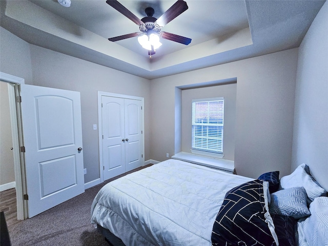 bedroom with ceiling fan, a raised ceiling, carpet floors, and a closet