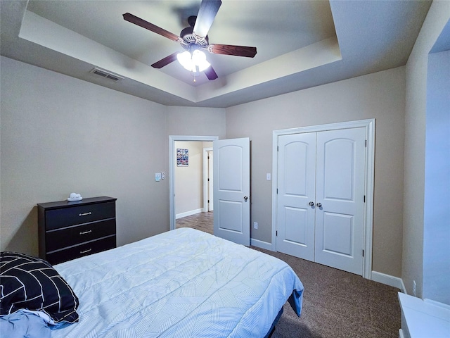 bedroom featuring ceiling fan, dark carpet, a raised ceiling, and a closet