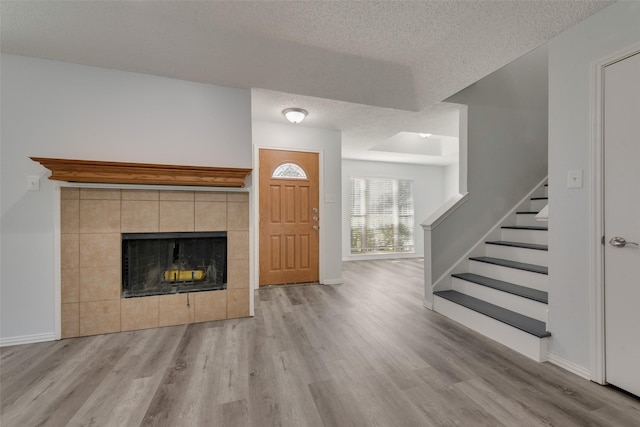 unfurnished living room with a tile fireplace, a textured ceiling, and light wood-type flooring