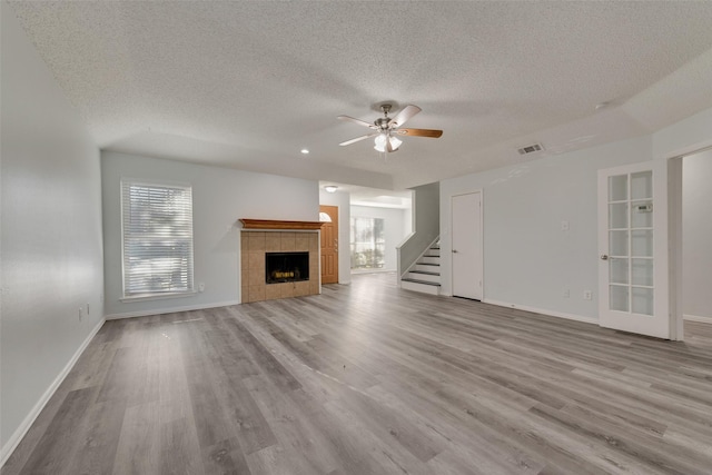 unfurnished living room with ceiling fan, light hardwood / wood-style floors, a textured ceiling, and a tiled fireplace