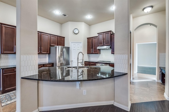 kitchen with sink, dark stone countertops, backsplash, dark brown cabinetry, and stainless steel appliances