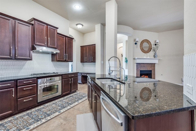 kitchen featuring dark stone countertops, sink, a center island with sink, and appliances with stainless steel finishes