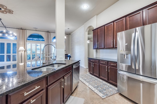 kitchen with sink, hanging light fixtures, light tile patterned floors, appliances with stainless steel finishes, and dark stone counters