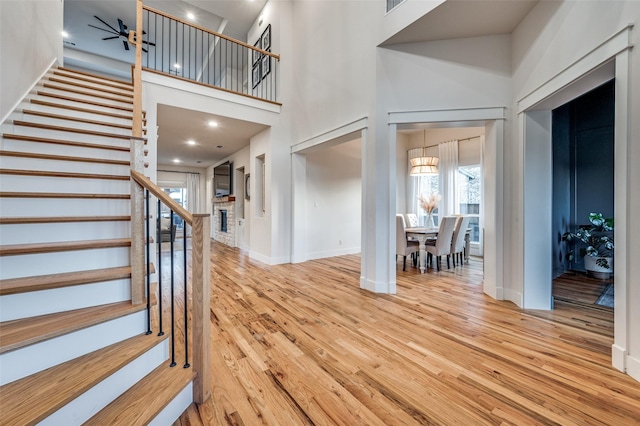 entryway featuring baseboards, stairway, wood finished floors, a high ceiling, and a fireplace