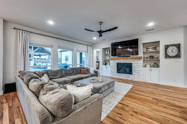 living room featuring ceiling fan, a fireplace, wood-type flooring, and built in features