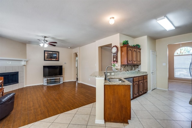 kitchen featuring kitchen peninsula, light stone countertops, sink, light tile patterned floors, and a tiled fireplace