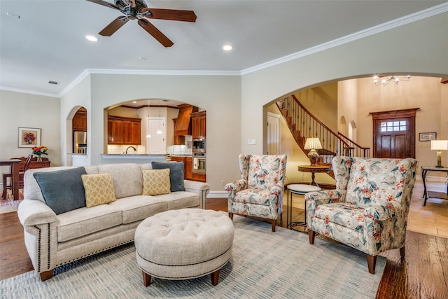 living room with light hardwood / wood-style flooring, ceiling fan with notable chandelier, and ornamental molding