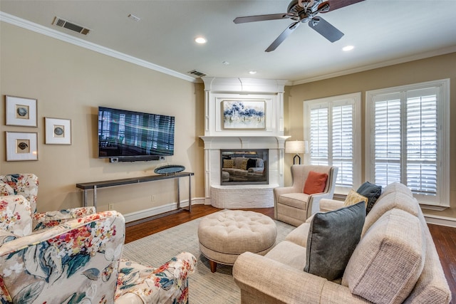 living room with a fireplace, dark hardwood / wood-style flooring, ceiling fan, and crown molding