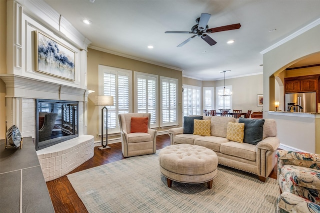 living room with ceiling fan, ornamental molding, dark wood-type flooring, and a brick fireplace