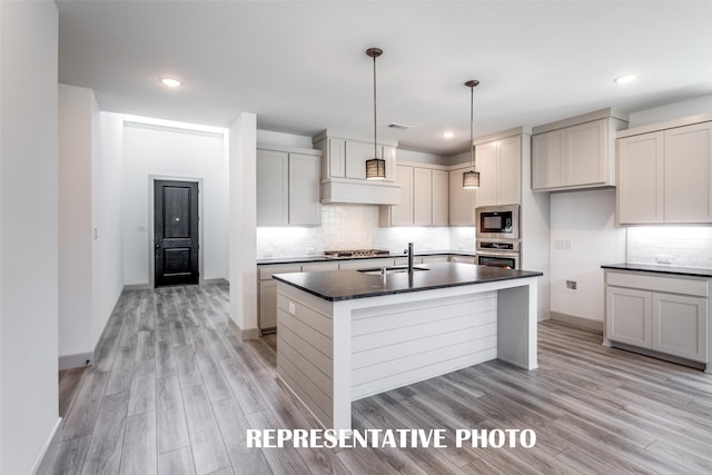 kitchen with sink, hanging light fixtures, light hardwood / wood-style floors, stainless steel appliances, and a center island with sink