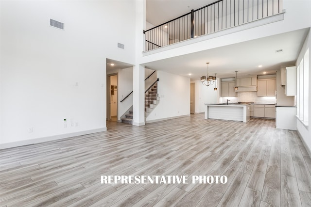 unfurnished living room featuring an inviting chandelier, a towering ceiling, and light hardwood / wood-style floors