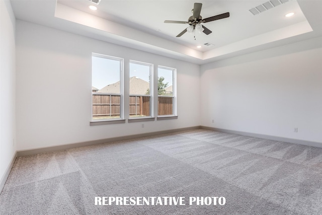 unfurnished room with light colored carpet, ceiling fan, and a tray ceiling