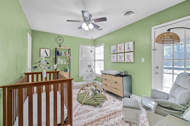 bedroom featuring a textured ceiling, a nursery area, and ceiling fan