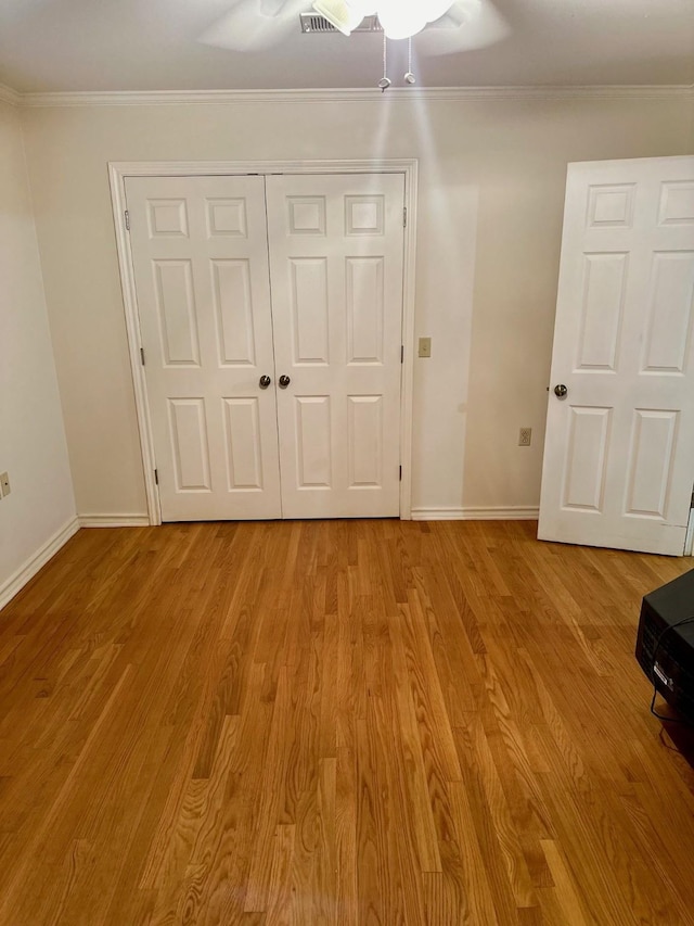 unfurnished bedroom featuring crown molding, light wood-type flooring, and a closet