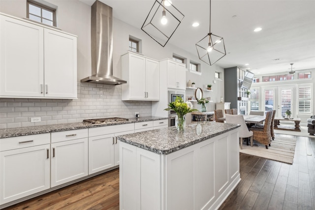 kitchen with pendant lighting, a center island, white cabinets, wall chimney range hood, and appliances with stainless steel finishes