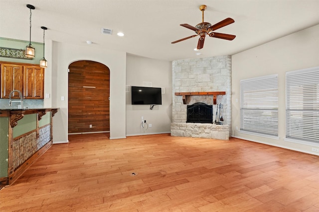 unfurnished living room with light hardwood / wood-style floors, a stone fireplace, ceiling fan, and sink