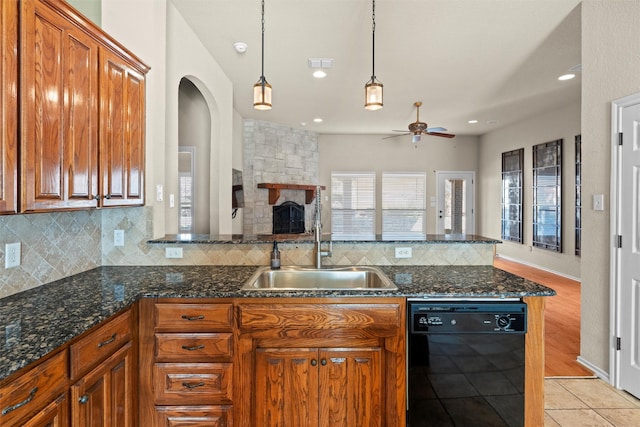 kitchen featuring ceiling fan, dishwasher, sink, backsplash, and a fireplace