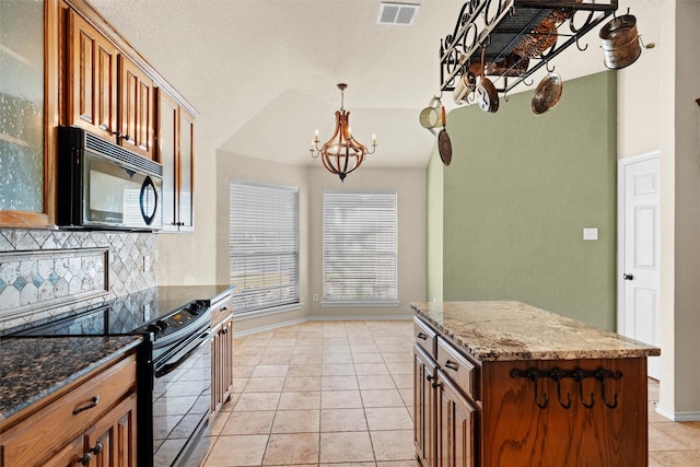 kitchen with a center island, dark stone counters, black appliances, light tile patterned floors, and a chandelier