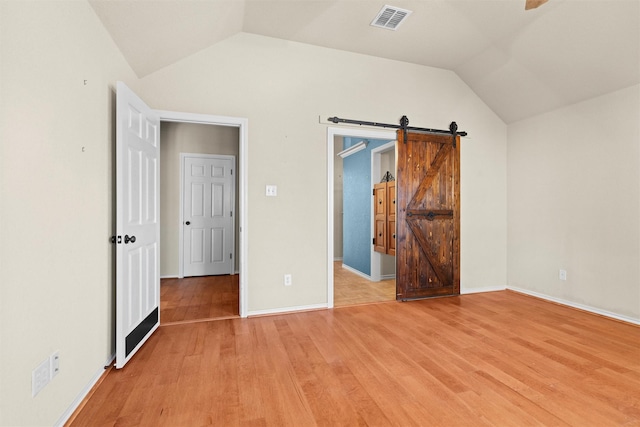 unfurnished bedroom with a barn door, vaulted ceiling, and light wood-type flooring