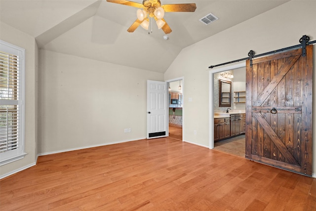 unfurnished bedroom with a barn door, light hardwood / wood-style floors, ensuite bath, and ceiling fan