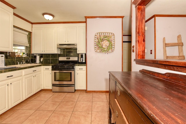 kitchen featuring ornate columns, light tile patterned floors, stainless steel gas range oven, decorative backsplash, and white cabinets