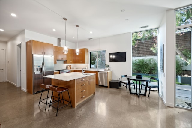 kitchen with backsplash, stainless steel appliances, decorative light fixtures, a breakfast bar area, and an island with sink