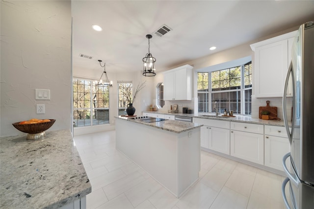 kitchen with light stone countertops, white cabinetry, a center island, stainless steel appliances, and decorative light fixtures