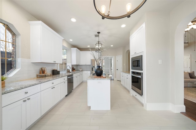 kitchen with decorative backsplash, stainless steel appliances, decorative light fixtures, a center island, and white cabinetry