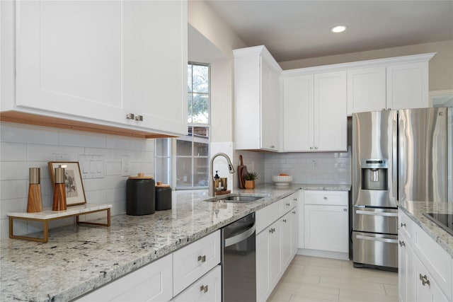 kitchen with backsplash, white cabinets, sink, appliances with stainless steel finishes, and light stone counters