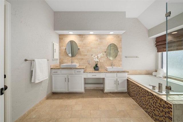 bathroom with a relaxing tiled tub, vanity, and vaulted ceiling