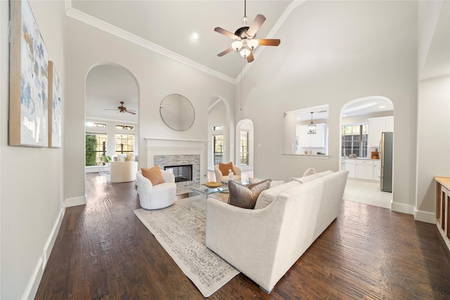 living room with dark wood-type flooring, crown molding, ceiling fan, a towering ceiling, and a fireplace