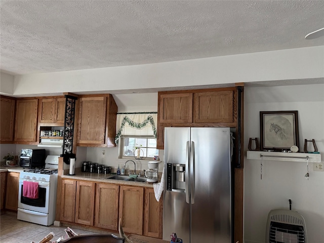 kitchen with sink, heating unit, stainless steel fridge, light tile patterned floors, and white gas range oven