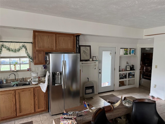 kitchen with sink, heating unit, stainless steel fridge, a textured ceiling, and light tile patterned floors