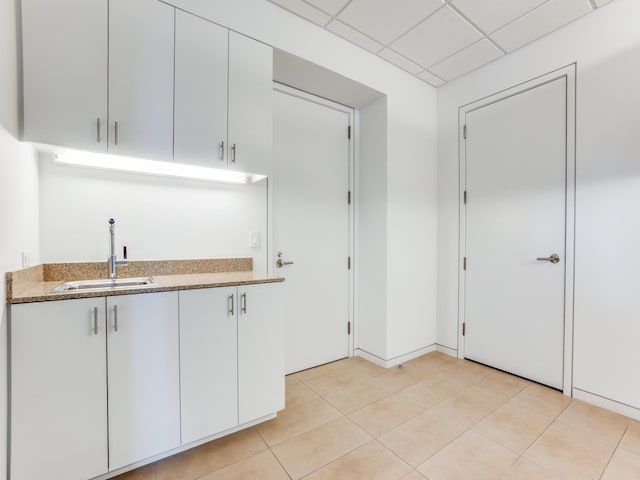 kitchen featuring a paneled ceiling, light stone counters, sink, light tile patterned floors, and white cabinetry