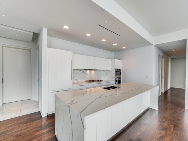 kitchen with white cabinets, a center island with sink, sink, tasteful backsplash, and light stone counters