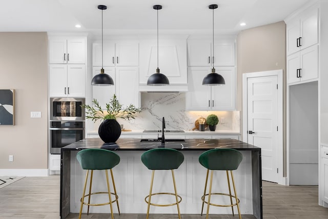 kitchen with white cabinetry, an island with sink, decorative backsplash, hanging light fixtures, and stainless steel appliances