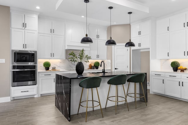 kitchen with hanging light fixtures, an island with sink, white cabinets, built in microwave, and oven