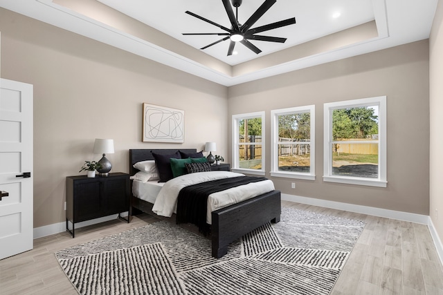 bedroom with ceiling fan, light hardwood / wood-style floors, and a tray ceiling