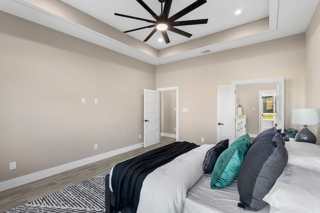 bedroom featuring light hardwood / wood-style floors, a raised ceiling, ceiling fan, and ensuite bathroom