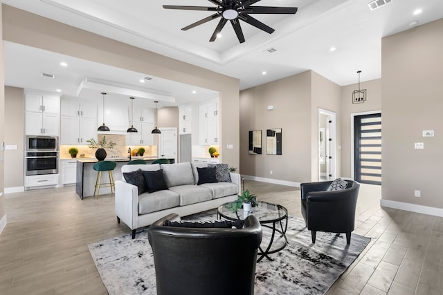 living room featuring a tray ceiling, a towering ceiling, ceiling fan, and light wood-type flooring