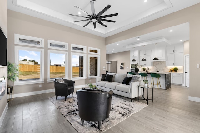 living room with light hardwood / wood-style floors, a raised ceiling, ceiling fan, and sink