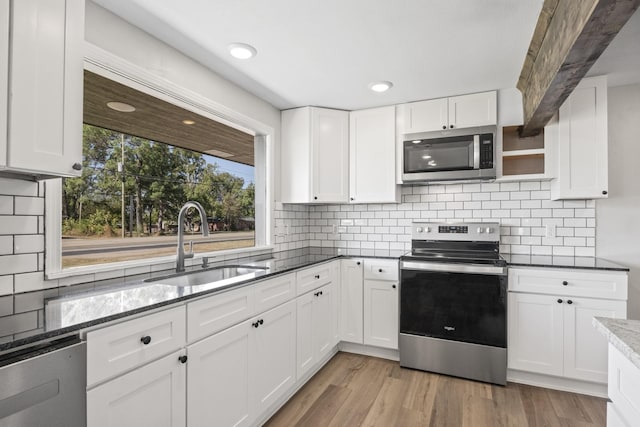 kitchen with sink, stainless steel appliances, dark stone countertops, white cabinets, and light wood-type flooring