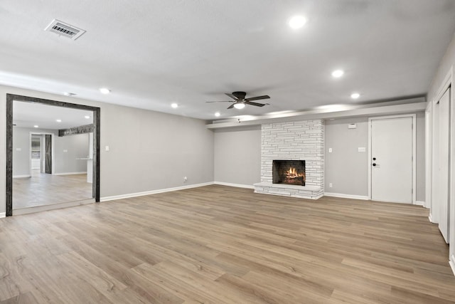 unfurnished living room with ceiling fan, a large fireplace, and light wood-type flooring