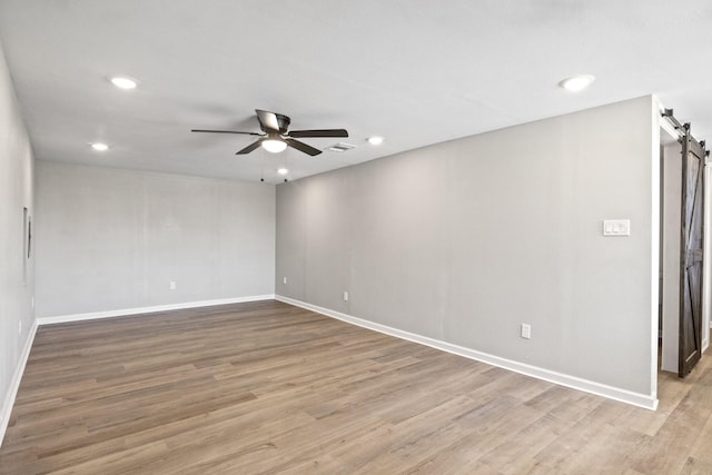 spare room featuring hardwood / wood-style floors, a barn door, and ceiling fan