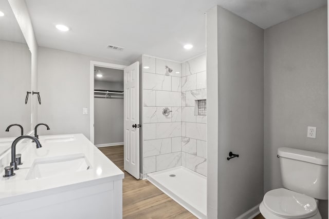 bathroom with hardwood / wood-style flooring, toilet, a tile shower, and vanity