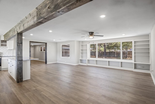 unfurnished living room featuring built in shelves, dark hardwood / wood-style flooring, and ceiling fan