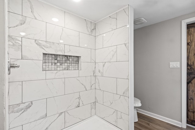 bathroom featuring hardwood / wood-style flooring, toilet, and tiled shower