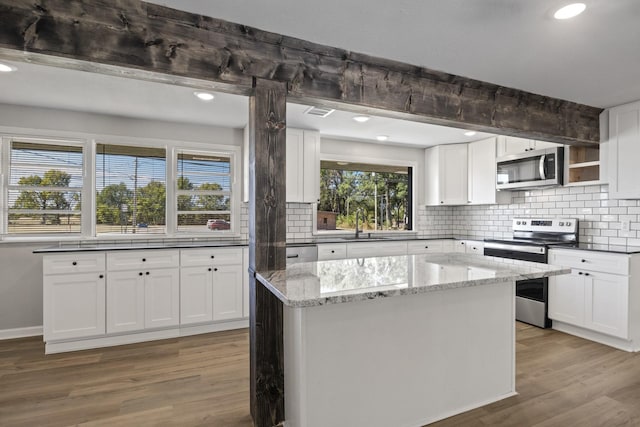 kitchen with white cabinets, light hardwood / wood-style flooring, dark stone countertops, a kitchen island, and stainless steel appliances